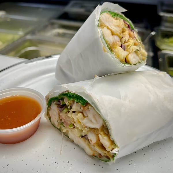 Two large Machete Taqueria burritos, wrapped in white paper, with a side of orange sauce.
