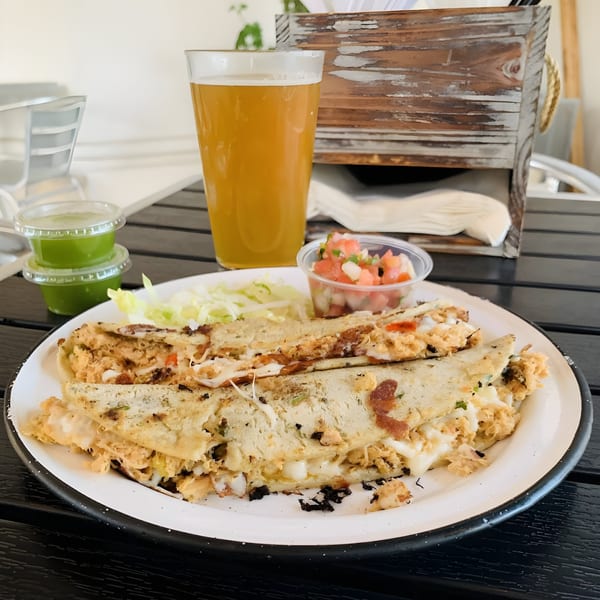 Chicken quesadillas with pico de gallo, shredded lettuce, green sauce, and a beer on a black table.